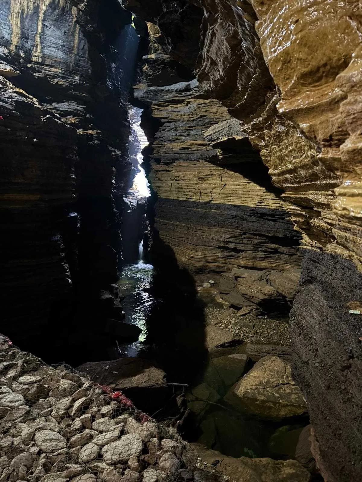 A sunlit passage inside the cave showing jagged layered rock walls and a small underground stream