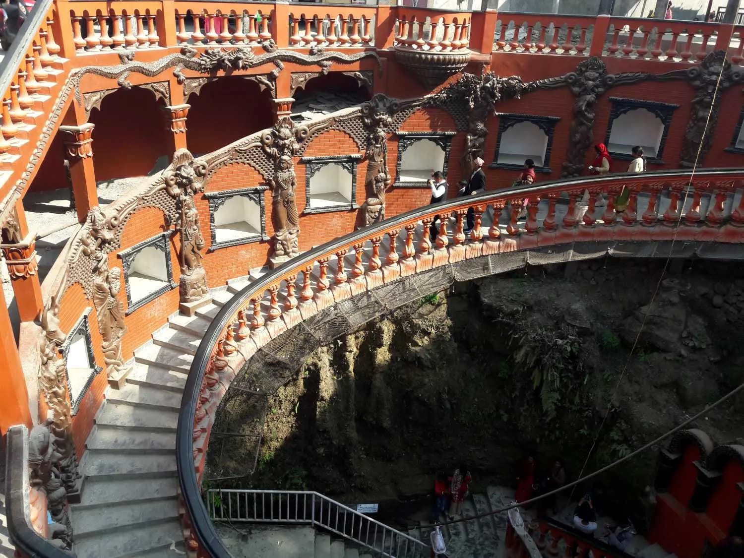 Ornate spiral staircase entrance to Gupteshwor Mahadev Cave featuring intricate carvings and red brick walls