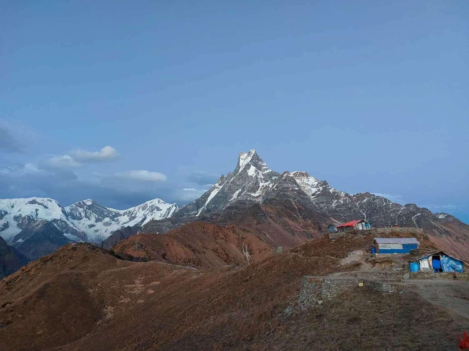 High altitude tea houses on a brown ridge with a view of Machhapuchhre in the distance