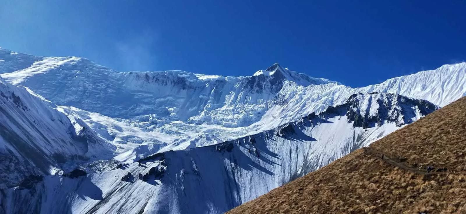 Vast snow-covered mountain ridges and glacial peaks under a bright blue sky on the Annapurna Circuit