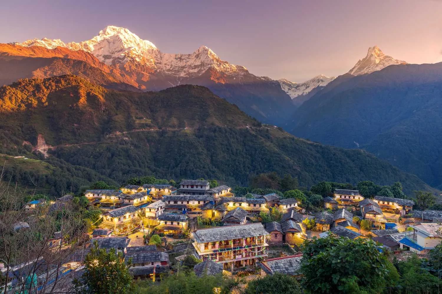 Ghandruk village glowing with lights at twilight beneath the golden peaks of Annapurna and Machhapuchhre